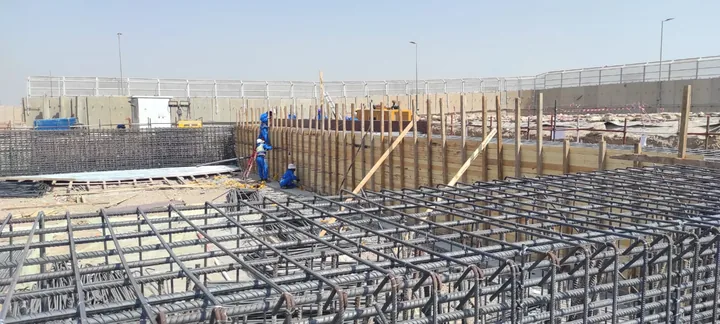 شبكات وقضبان حديد تسليح أمام شدات خشبية في موقع العمل.