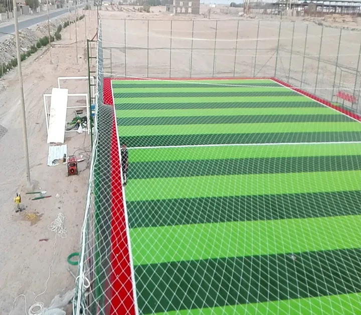 ملعب مستطيل بعشب صناعي مخطط محاط بشباك وسياج.