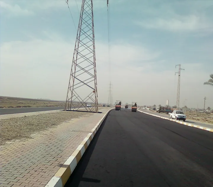 طريق أسفلتي بمحاذاة رصيف مبلط وحواجز حافة خرسانية.
